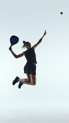 Female padel player jumping for powerful overhead shot on white background. Concept of professional...