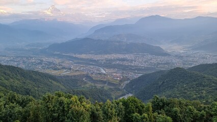 Fototapeta premium Misty Mountain Landscape Overlooking Pokhara Town at Sunrise with Hazy Sky and Lush Green Hills