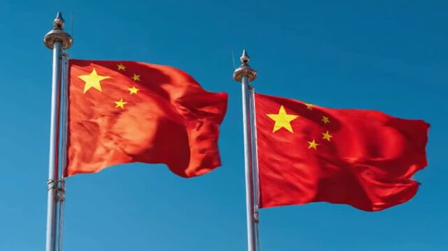 Two vibrant red flags, each adorned with a distinctive pattern of yellow stars, wave majestically in a gentle breeze against a clear, azure blue sky. The flags' rich colors and dynamic movement evoke 