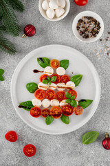 Festive Christmas Caprese salad with cherry tomatoes, mini mozzarella, and fresh basil served on a plate, styled in the shape of a Christmas tree for holiday celebrations. Top view.
