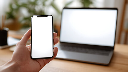 Hand holding smartphone with blank screen next to open laptop white screen
