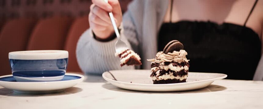 Close-up view of hands holding a fork and eating cake in a cafe, handheld shot with anamorphic lens effect, soft focus, warm colors and intimate cafe atmosphere.