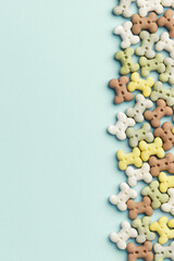 A colorful bone-shaped dog treats in pastel shades aligned scattered on a soft blue background.