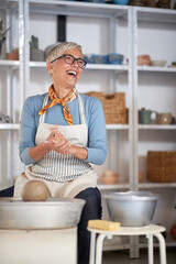 Happy elderly woman making pot from clay in studio.