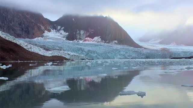A glacial landscape shows icebergs in still waters, reflected from a towering glacier under cloudy skies near mountainous regions in Arctic conditions.