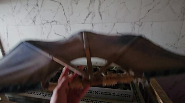 Person is holding a blue and white kite fan felled in sauna near oven. The kite is made of a thin material and has a wooden frame