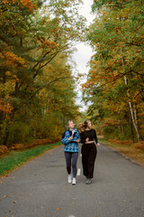 Fototapeta premium Two friends stroll through a peaceful forest path lined with vibrant autumn trees. Their laughter fills the air as they enjoy the crisp, cool weather together.