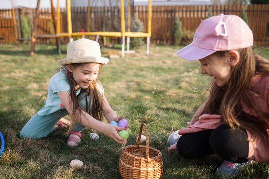 spring fun - finding eggs for easter outdoor in countryside. Happy children sitting on grass with found eggs and put them in a basket on sunny day. easter hunt in backyard.