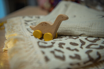 lose-up of a Wooden Brontosaurus Toy with Yellow Wheels on a Leopard Print Blanket.  Eco-Friendly Baby Toy: Handmade Wooden Dinosaur on Cozy Fringed Textiles. Nursery Decor Detail: Montessori-Style  © Александра Царивская