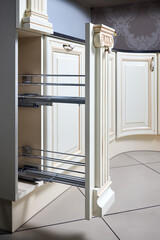 Pull out spice rack cabinet filler pantry. Interior of modern kitchen in classic style with golden elements in beige colors. Vertical drawer for spices shelf under countertop with front wooden panel.