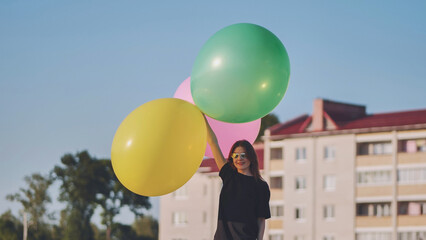 A girl happily poses with large with colorful balloons in the city.