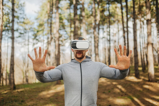 Virtual reality experience in a forest setting with a man using goggles and standing with hands raised