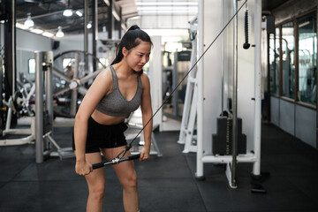 Fototapeta premium Fit female athlete in gray sports bra and black shorts exercising with resistance cables. Healthy lifestyle and wellness concept.