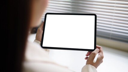 Close up of woman holding digital tablet with blank white screen in modern office. Mockup space for design, website, or app presentation.