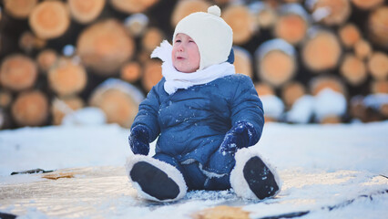 Bundled infant resting on snowy wooden surface near stacked firewood during cold winter season