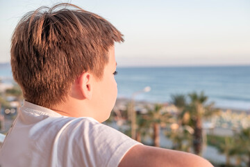 Fototapeta premium young preteen boy gazing ocean horizon from balcony, golden hour, serene moment contemplation against coastal backdrop, quiet reflection seaside, childhood vacation memory, nature discovery moment