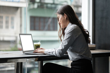 Professional businesswoman sitting by the window, typing on her laptop with a clean white display
