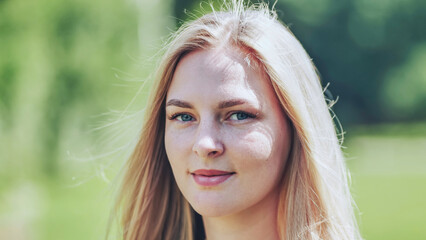Blonde woman with freckles smiling, enjoying sunny summer park setting