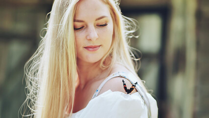 Serene blonde woman experiencing delicate butterfly perching gently on shoulder amid lush garden landscape