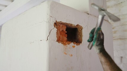 Construction worker breaking white wall with hammer revealing bricks
