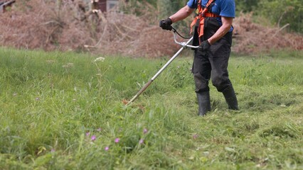A man mows the grass with a trimmer on a summer day.