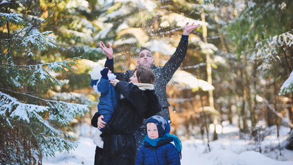 Cheerful family tossing snowflakes, enjoying winter moments amid snow covered woodland landscape