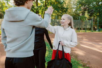 Fototapeta premium Joyful players share a high-five after a spirited game on a red clay court. The sun shines through the trees, creating a warm atmosphere as they enjoy their time together.