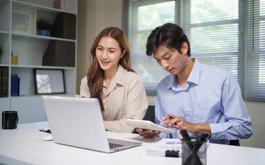 Obraz premium Two young professionals working together at a desk, reviewing financial data on a laptop and calculator.