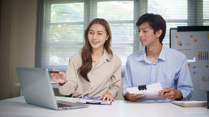 Obraz premium Smiling business team discussing numbers and checking calculations while using a laptop.