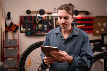 Small business owner using digital tablet while working in bicycle repair shop or garage