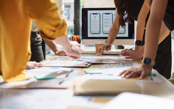 UX UI design team collaborating around a table full of wireframes and mobile app prototypes.