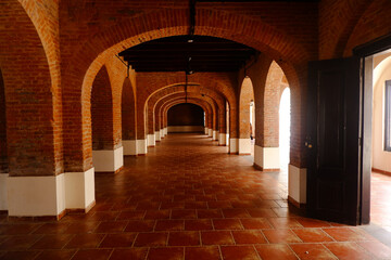 Fototapeta premium The corridor of an old building made of sturdy red brick. The long corridor forms a leading line. Perspective photo of the building. 