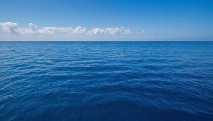 Fototapeta premium Waves roll gently across the calm ocean under a clear blue sky with a few clouds on a sunny day near the shore