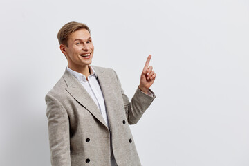 Confident smiling man in light grey blazer points upward on plain white background, casual business attire, friendly expression, professional pose, clean studio shot, ideal for corporate, marketing or