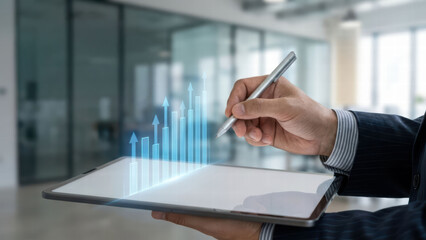 Person in suit uses stylus on digital tablet displaying rising bar graph, symbolizing digital business growth. background is modern office setting