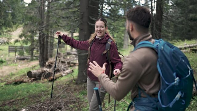 A young couple hiking through a forest with backpacks and walking sticks, enjoying nature and outdoor adventure.