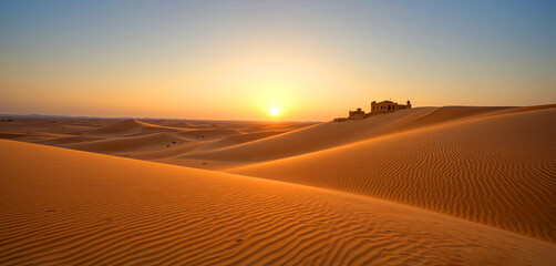 Sunset over sand dunes with an old building in the desert landscape of a vast sandy area