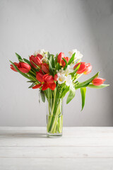 Spring floral background. Red tulips and Fresia white flower bouquet in glass vase. Copy space