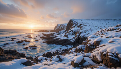 Snow covers rocks by the ocean as the sun sets behind the cliffs during winter at the coast