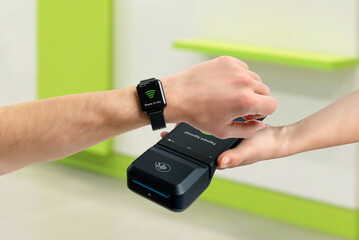 Customer paying with smart watch using contactless POS terminal indoors, demonstrating tap payment, wearable technology, digital transaction, and modern retail checkout process