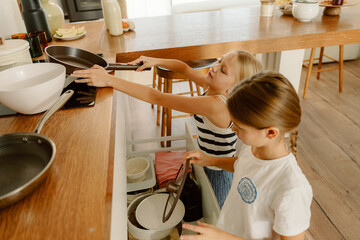 In a cozy, well-lit kitchen, two young girls collaborate to prepare a meal. They joyfully reach for pots and pans, showcasing teamwork and creativity in their culinary adventure.