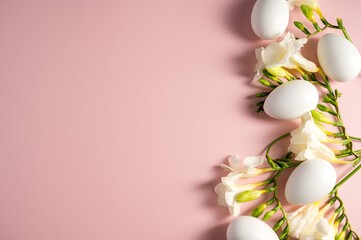 Easter holiday background. Freesia white flowers and white easter eggs on pink background, flat lay with copy space