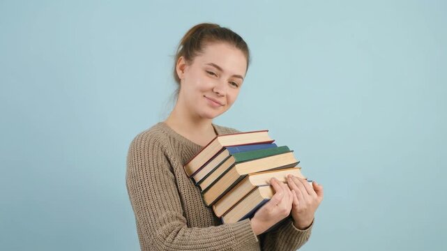 Happy young caucasian female student holding a heavy stack of books for studying. Smiling bookworm enjoying literature and preparing for college exams as a learning concept