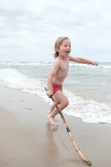 Radosne dziecko bawiące się patykiem na plaży nad morzem podczas letnich wakacji © Przemysaw