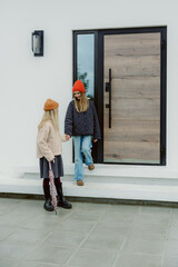 Fototapeta premium Outside a contemporary house, two cheerful girls connect as they descend the steps. Dressed in cozy winter attire, they share smiles, showcasing a bond of friendship on a chilly day.