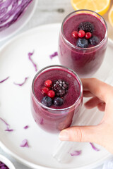 Hand is holding red cabbage berry smoothie. Top view. Healthy blended drink for breakfast.