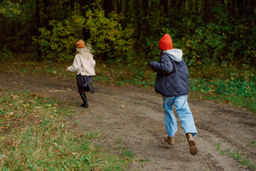 Fototapeta premium Two young girls dash along a dirt path in a vibrant forest, surrounded by tall trees and fresh greenery. Their joyful energy is evident as they enjoy a playful adventure outdoors.