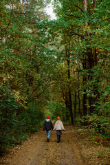 Fototapeta premium Two people stroll together along a scenic forest trail, surrounded by tall trees and vibrant foliage. The serene atmosphere creates a feeling of peace and connection to nature.