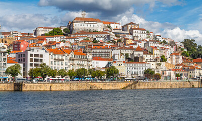 Beautiful view of the University of Coimbra perched on the hill above the historic old town buildings and riverfront on a bright sunny day.