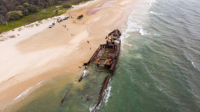 Aerial view of the rusted shipwreck of the SS Maheno lying on the beach, where the golden sand meets the turquoise water, Fraser Island, Queensland, Australia.